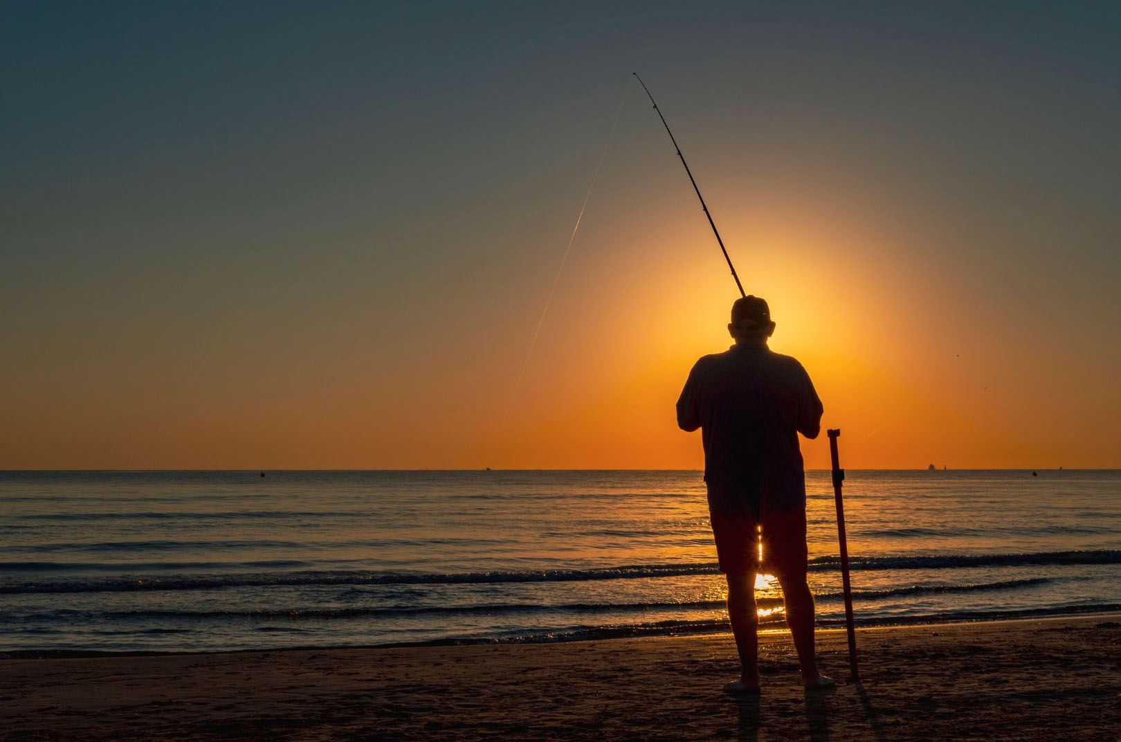 Man fishing from beach at sunset.